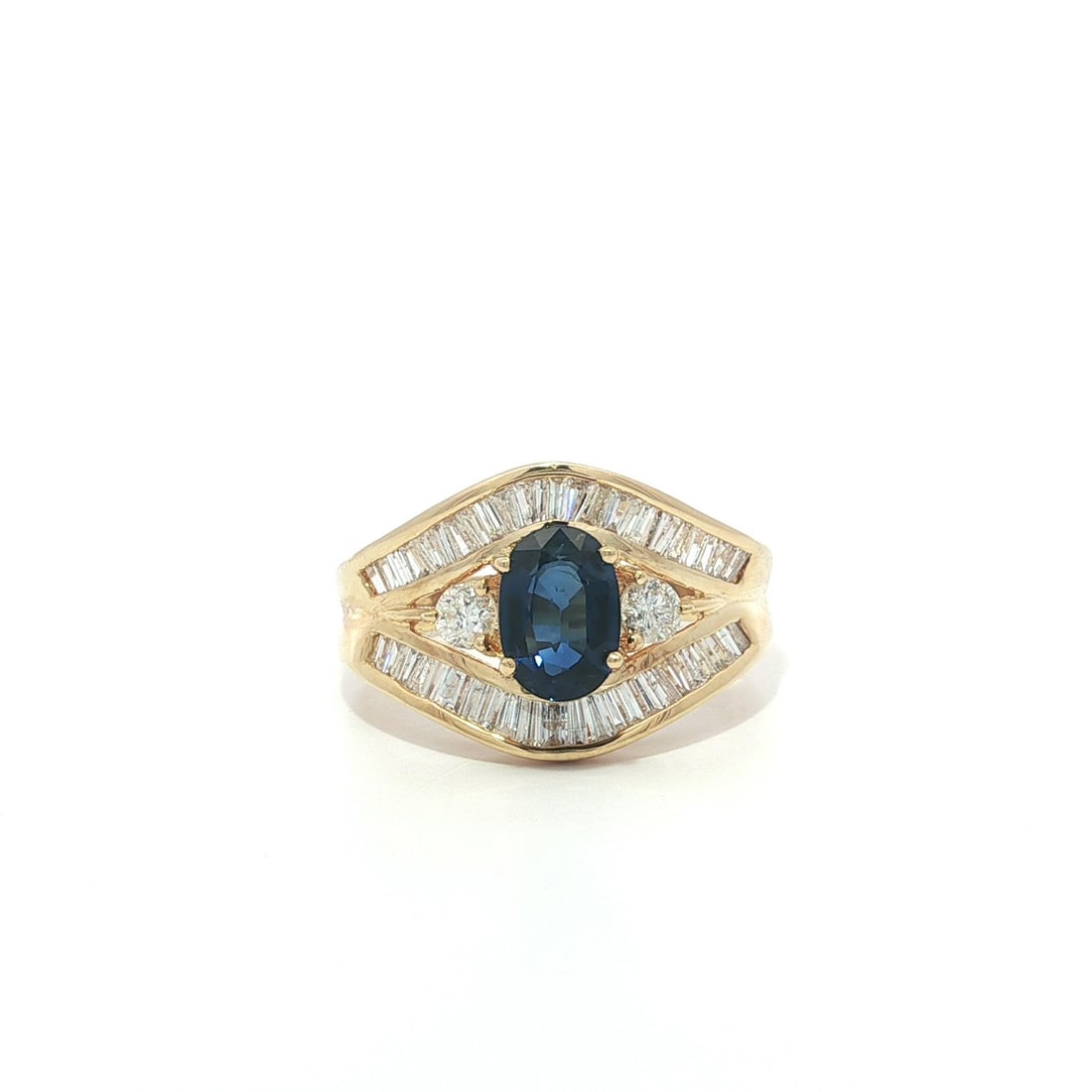 Cocktail Ring in 18k Yellow Gold with Blue Sapphire and Diamond Baguettes: Cocktail Ring in 18k Yellow Gold with Blue Sapphire and Diamond Baguettes This statement cocktail ring features a deep royal blue oval-cut natural sapphire, complemented by numerous baguette-cut natur