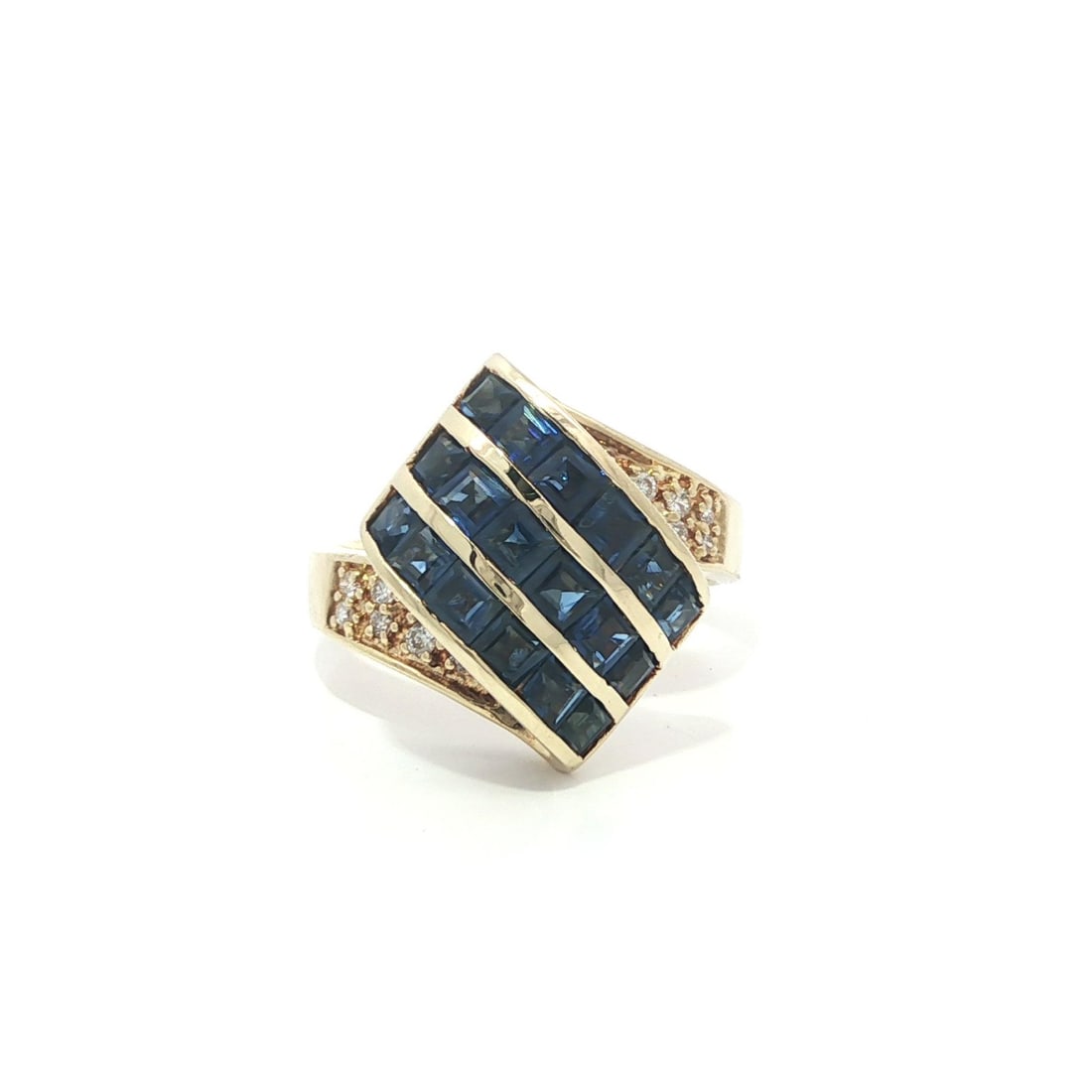 Cocktail Ring in 14k Yellow Gold with Blue Square Sapphires and Pave Diamonds: Cocktail Ring in 14k Yellow Gold with Blue Square Sapphires and Pave Diamonds This cocktail ring features a ribbon-like design crafted from solid 14k yellow gold. It is set with approximately 3.0 cara