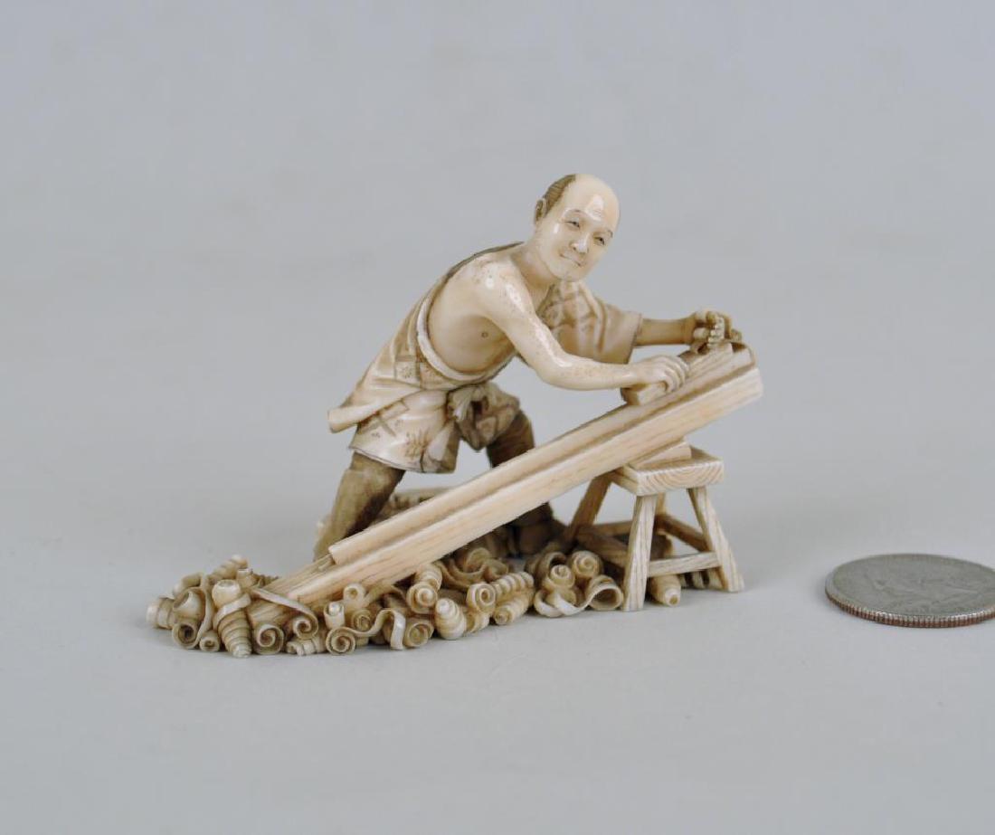 Japanese Carving of Woodworker: planing a board, with wood shavings at his feet, signed on bottom. A couple small age cracks and a few small greenish stains to base. 2 1/4" high, 3 1/4" wide. International clients may be ineligible 