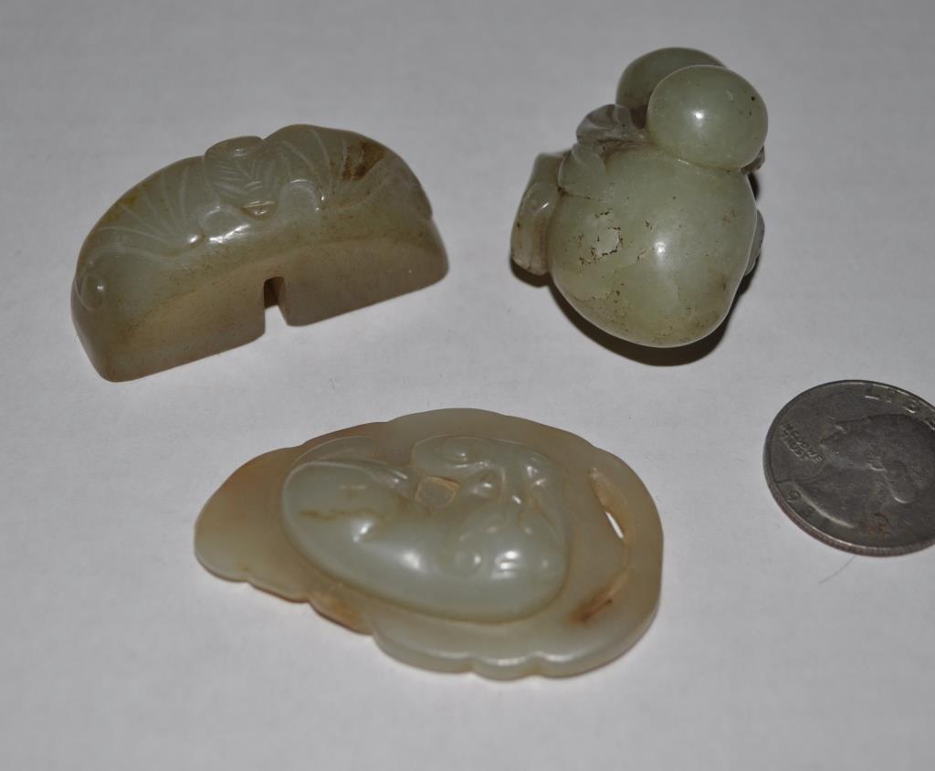 Three Chinese Celadon Jade Carvings: comprising a double seal with bat motif, a reclining cat on a leaf base, and a pebble form group of fruit. Largest: 3/4" high, 1 7/8" wide, 5/8" deep.