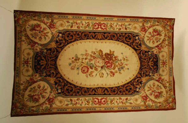 Handmade Needlepoint Rug: Handmade needlepoint rug/wall hanger made in the USA, Durham NC. Beige oval center with black bordering with rust border, roses set in ovals and leafage. In good condition. 59" long, 36" wide.