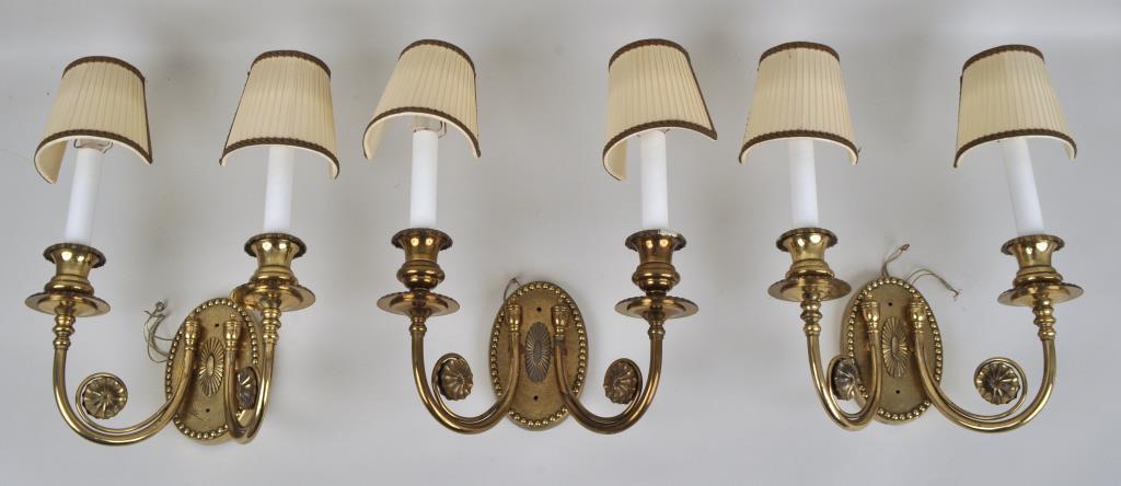 Group Three Neoclassical Style Brass Wall Sconces: two arm form, oval backs with raised paterae. 15" high, 10" wide, 5 1/2" deep. With shades. Provenance: Property of a Fairfield County Collector.