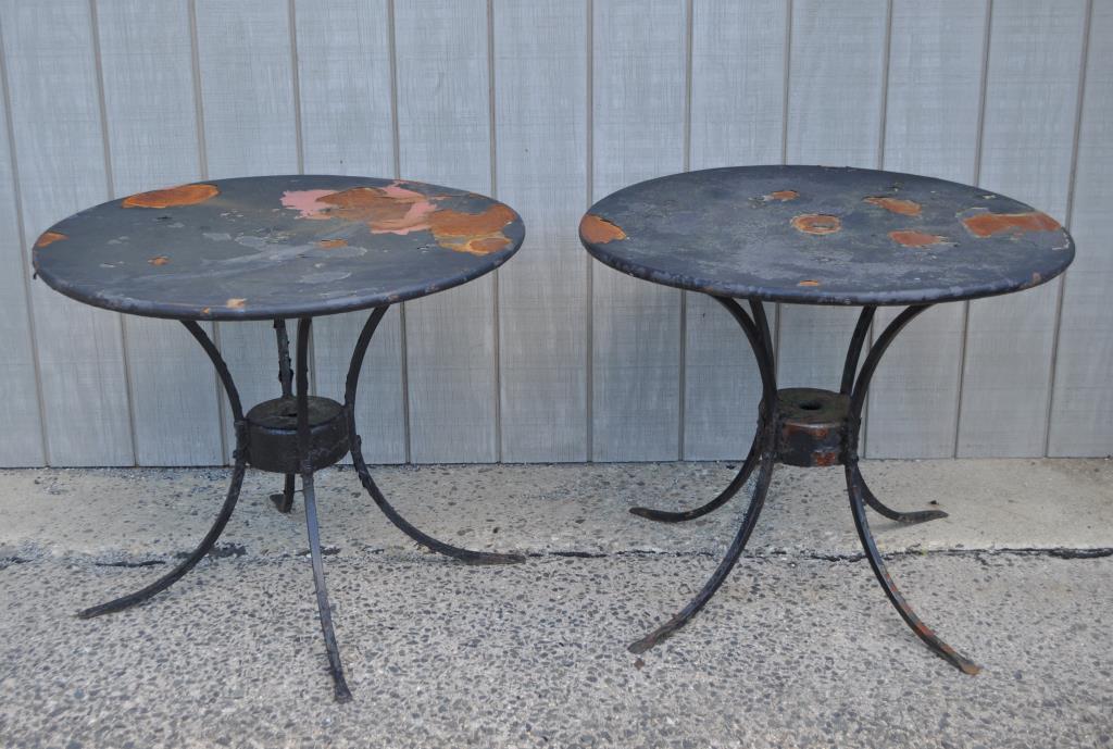 Two Wrought Iron Round Garden Tables: with sheet metal tops and four curved wrought iron legs. 26 7/8" high, 33" diameter at the top. Substantial paint loss and flaking. Provenance: Property of a Massachusetts Institution.