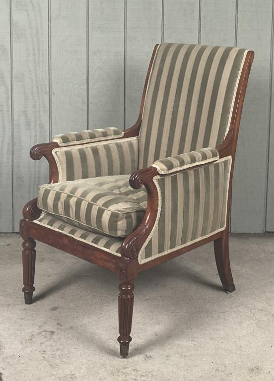 Regency Carved Mahogany Upholstered Bergere Chair: with carved arms and posts, reeded legs with brass feet. 40 1/2" high, 27 1/2" wide, 29" deep; seat height 19". Age and use wear to frame. Property from the Estates of Eve & Peter Mancino, Bridgewater