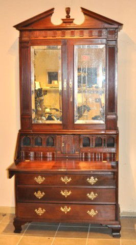 George III Mahogany Pitch Pediment Secretary: George III carved and figured mahogany two-part slant front secretary bookcase, with pitch pediment top, dentil molded pilaster detail and flame finial, above two rectangular doors fitted with beveled