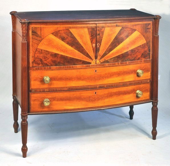 Sheraton Style Inlaid Mahogany Sideboard: Sheraton style inlaid mahogany bowfront server or sideboard, with figured mahogany top with concentric ring turned edge, having extruded corners above waterleaf carved capital continuing to reeded sti