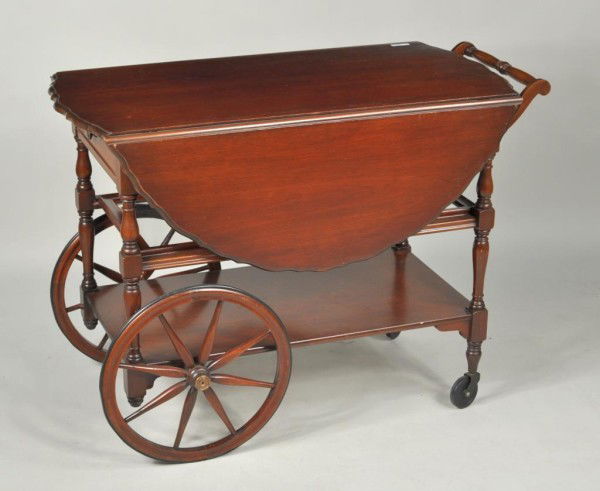 Sheraton Style Mahogany Wheeled Tea Table: Sheraton style mahogany wheeled tea cart with scalloped top and drop leaves, 20th century. 28 3/4" high, leaves up: 45" wide; leaves down: 20" wide, 37 3/4" deep.