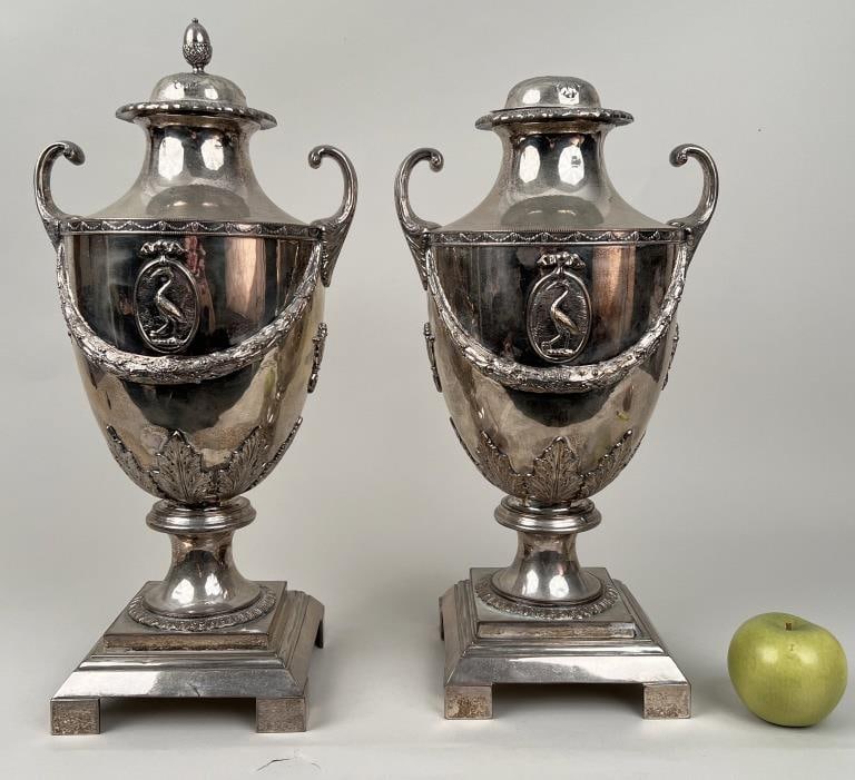 Pair Silver Plate Pistol Handled Neoclassical Urns: body of urns decorated with swags, festoons and oval medallions, lids with acorn finials. 19 1/2" high, 10" wide, 8" deep. Wear and oxidation, some nicks and scrapes, one with detached base and missin