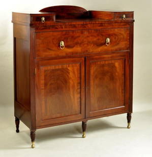 NY Classical Mahogany Server, Phyfe School: arched back-splash flanked by raised box drawers, case with one large top drawer above two cupboard doors between reeded pilasters, turned and reeded legs with brass ball feet, early 19th century. 56"