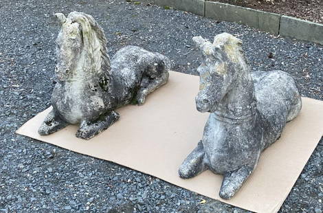 Pair Carved Concrete Reclining Horse Sculptures: depicted with decorative neck garlands, possibly Chinese origin. 21" high, 32" long, 12" deep. Losses and wear from exposure to elements, oxidation and soiling, loss to ear on one.