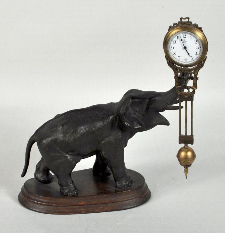 Jungans Elephant Swinging Clock: Jungans Elephant swinging clock, with brass pendulum and case with porcelain dial, simulated bronze elephant on an oval wood base. 11 1/2" high, 10" wide, 4 1/4" deep.
