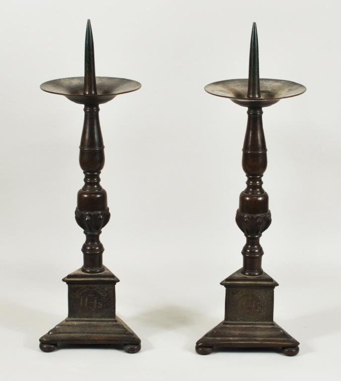 Pair Continental Footed Brass Pricket Sticks: Pair of turned brass/bronze pricket sticks, on triangular footed bases, the bases engraved with initials "MA" and "AN" over a heart and "IHS", probably Continental, 18th/19th century. Each 18" high, 6
