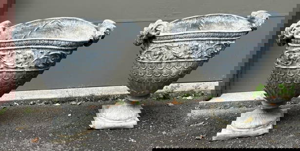Pair Neoclassical Lead Garden Urns, Ram Mounts: flattened ovoid shape, with scrolling leafage and scale ornament on bodies, rams horn end mounts, on square plinths. 30" high, 33" wide, 15" deep. Expected age and use wear, oxidation, soiling, some