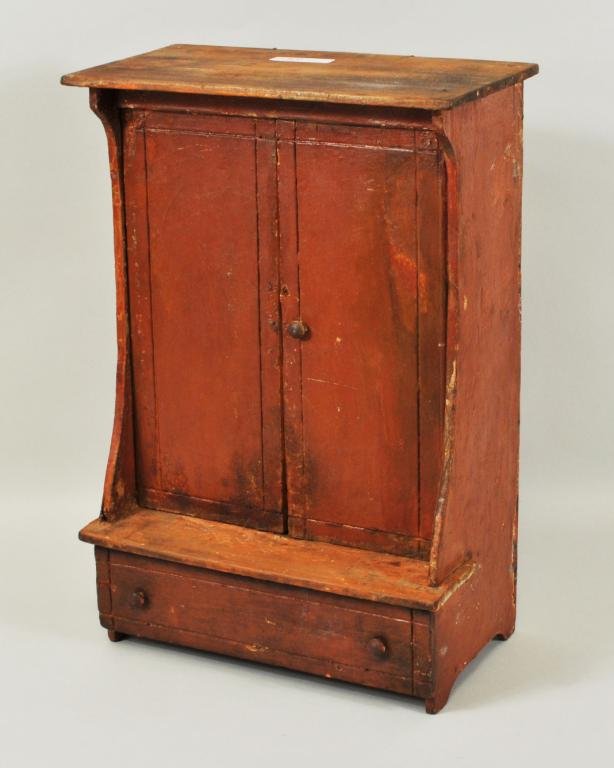 Miniature Red Painted Linen Press, 19th C.: Miniature red painted linen press, 19th C, two large doors above, on stepped base, long drawer below. 16 1/2" high, 11" wide. Condition: paint wear, loss, marring to top.