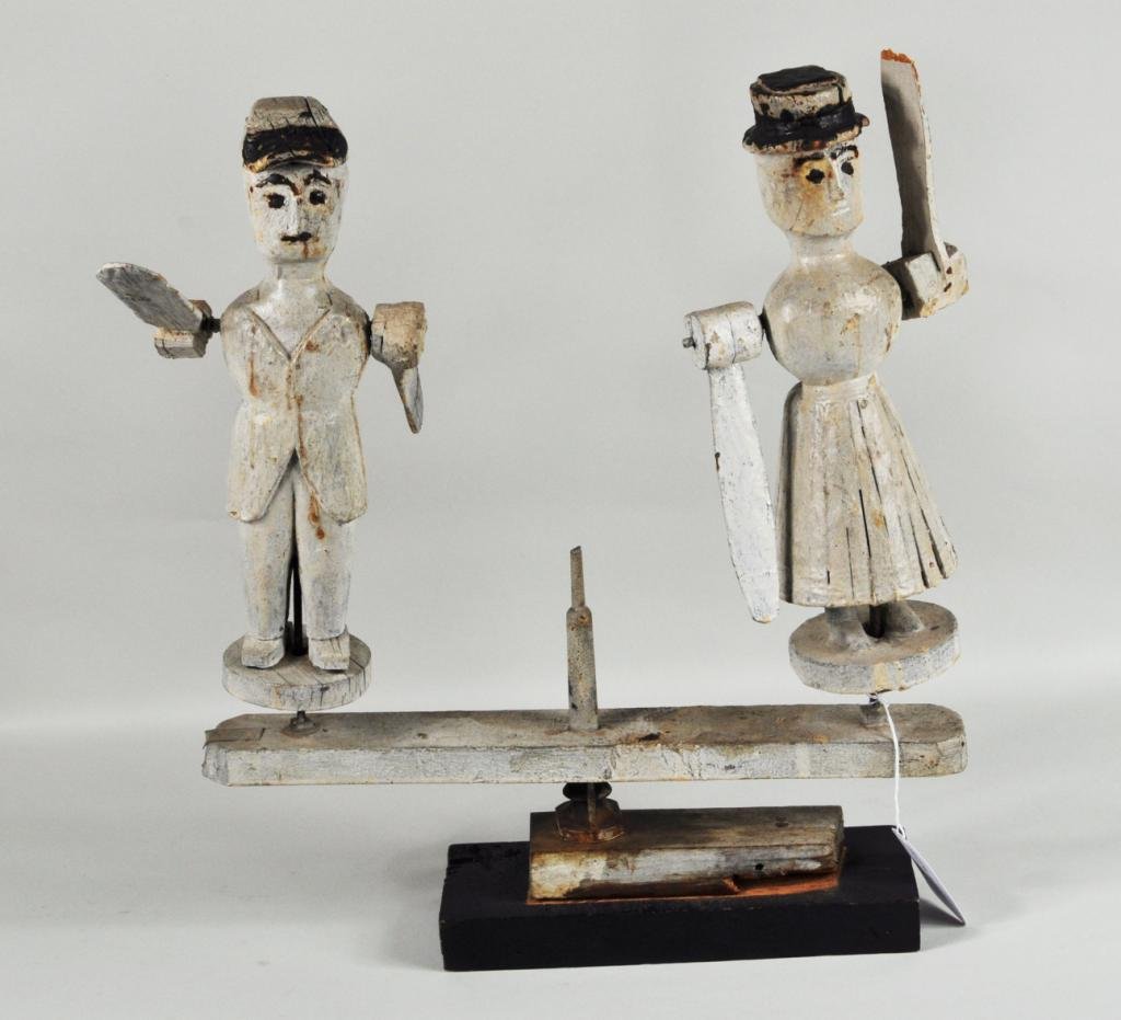 American Folk Art Carved/Painted Double Whirlygig: American folk art carved and painted double whirlygig, 19th/20th C., depicting a primitive couple in white paint with black detail having arm blades, on wood stand. 19" high, 19" wide. Condition: age 