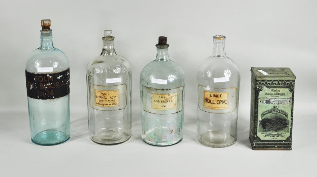 Four Large Apothecary Bottles: Four large apothecary bottles, 19th/20th C., with paper labels, together with a tole ware covered tin. Largest: 15" high, 5" diameter; smallest: 9" high, 4 1/2" wide, 4" deep. Provenance: The Aronson