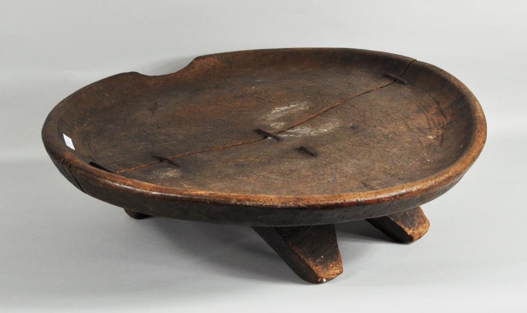African Carved Wood Footed Bowl: African carved wood footed bowl, 20th C., with old "make-do" stapled repairs. 6 1/2" high, 24" diameter. Condition: wear, worm damage, age cracks, losses.