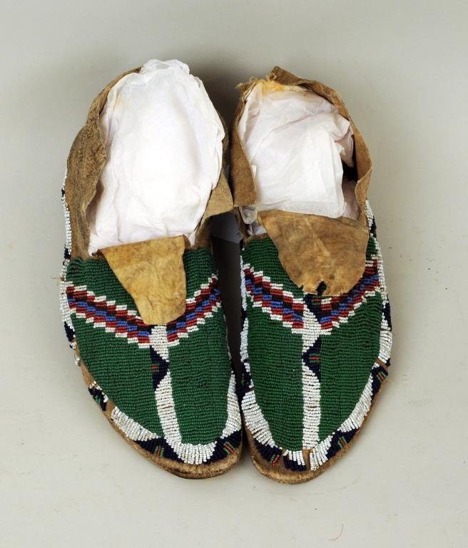 Pair of Plains Beaded Hide Moccasins: Pair of Plains beaded hide moccasins, 19th/20th century, tops with green, blue, red and white beadwork designs, 11" long, 4 1/4" wide. Condition: hide stiff, soiling, tears losses.