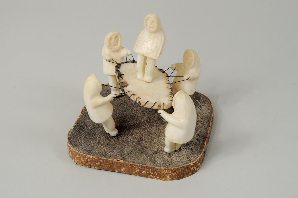 Inuit Carved Marine Ivory Sculpture: Inuit carved marine ivory sculpture depicting figures and sealskin trampoline signed on underside "Dwight Milligrock, Sr." 4 1/2" high, 4 1/4" wide.