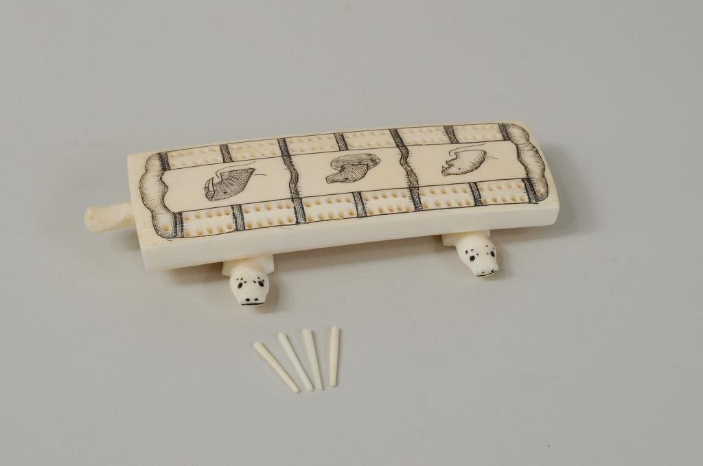 Small Inuit Scrimshaw Marine Ivory Cribbage Board: Small Inuit scrimshaw marine ivory cribbage board with four pegs, signed "Edward N Penatac." 3/4" high, 4 3/4" long.