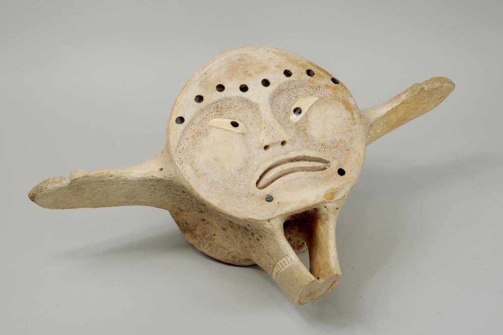 Inuit Carved & Inlaid Whalebone Vertebra Sculpture: Inuit carved and inlaid whalebone vertebra sculpture, one side depicting a stylized face, verso depicting a man, hands in the form of animal heads, initialed "BJ" under arm. 9 1/2" high, 17" wide.