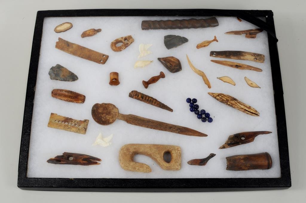 Group of Inuit Carved Fossilized Tools: Group of Inuit carved fossilized tools and other items including a spoon, hook and several items with incised decoration presented in a riker case. 1/4" diameter to 7 1/4" long, 1 1/2" wide.