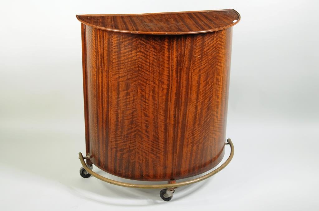 Modernist Lithographed Metal Demilune Bar: Modernist lithographed metal demilune bar on wheels with faux grained wood finish, one interior shelf and fitted lower section for bottles. 33" high, 30" wide, 16" deep. Condition: scratches, finish w