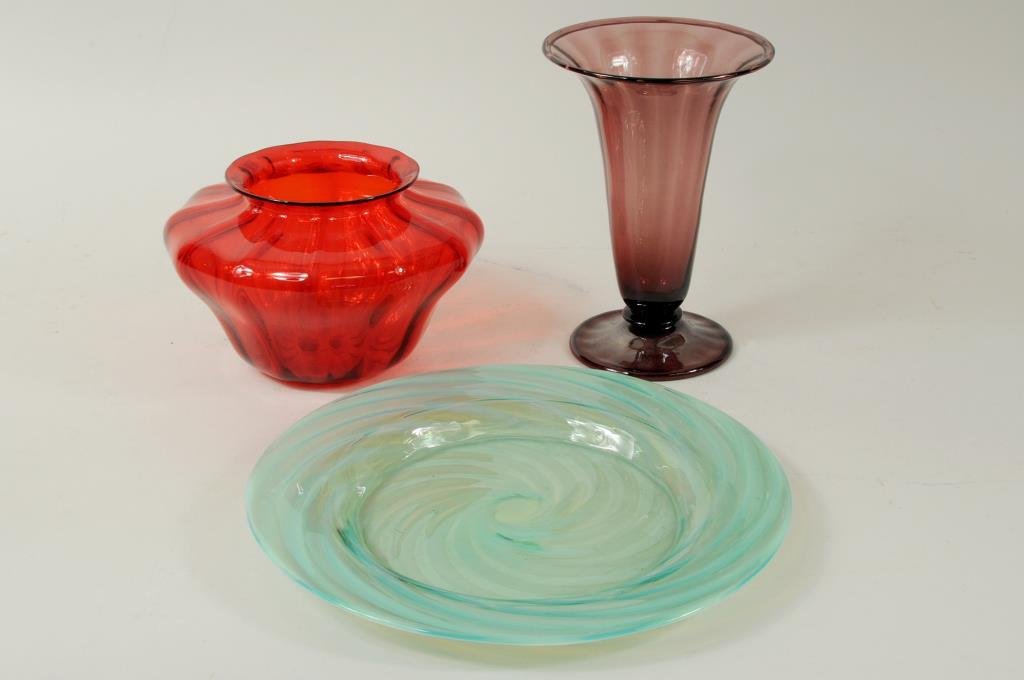 Three Colored Art Glass Items: Three colored art glass items comprising a Steuben amethyst ribbed vase with acid etched stamp on base, a green swirl form dish and a red ribbed glass vase, both unsigned. 6" high, 4" wide to 8 1/4" d
