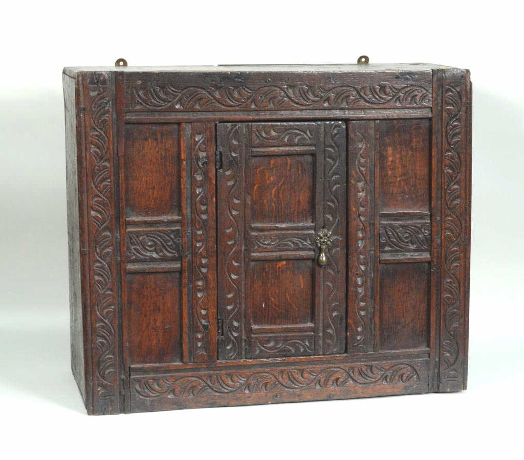 English Oak Hanging Wall Cupboard: English oak hanging wall cupboard with carved foliate detail. 20" high, 24" wide, 9 3/4" deep. Condition: wear, age cracks, losses.