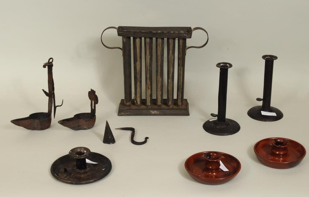 Group Eight Antique Lighting Items: Group of eight lighting items comprising two Betty lamps, a tin candle mold, three tin candlesticks and a pair of redware candle holders. 4" high, 4 1/2" wide to 9 1/2" high, 11" wide. Condition: use