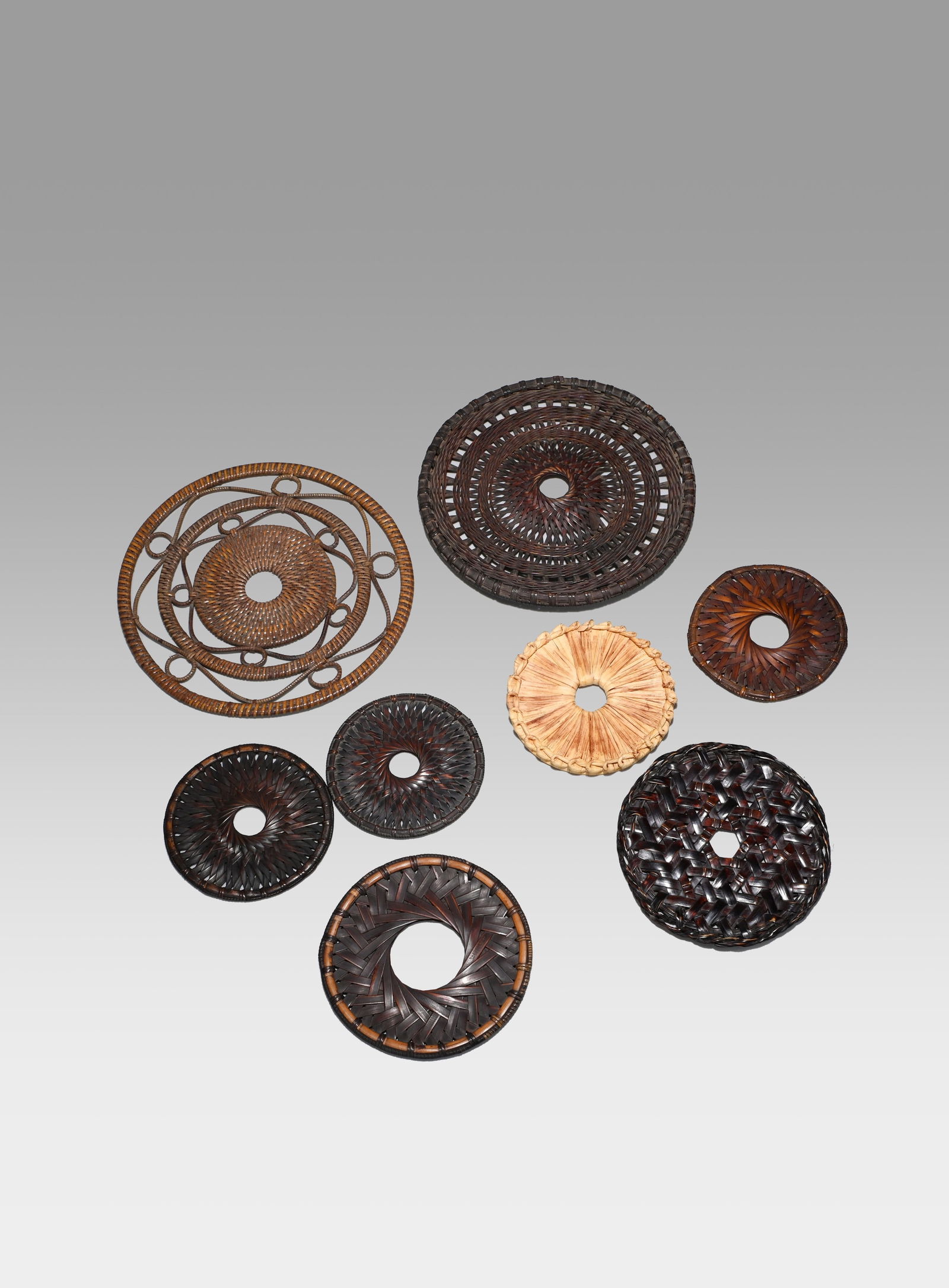Eight Bamboo Vase Stands: A set of eight finely woven bamboo trivets. Each piece, circular in form, demonstrates a variety of weaving techniques—radiating, interlaced, or openwork patterns—creating a rich visual diversity.