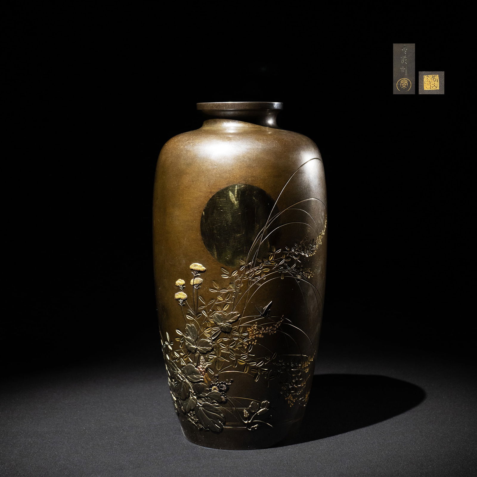 Gilt and Silver Inlaid Vase by Shokosai: A refined shibuichi vase of elegant ovoid form, its subtly patinated surface serving as a quiet ground for an elaborate autumn landscape rendered in high relief carving and gold and silver inlay. A