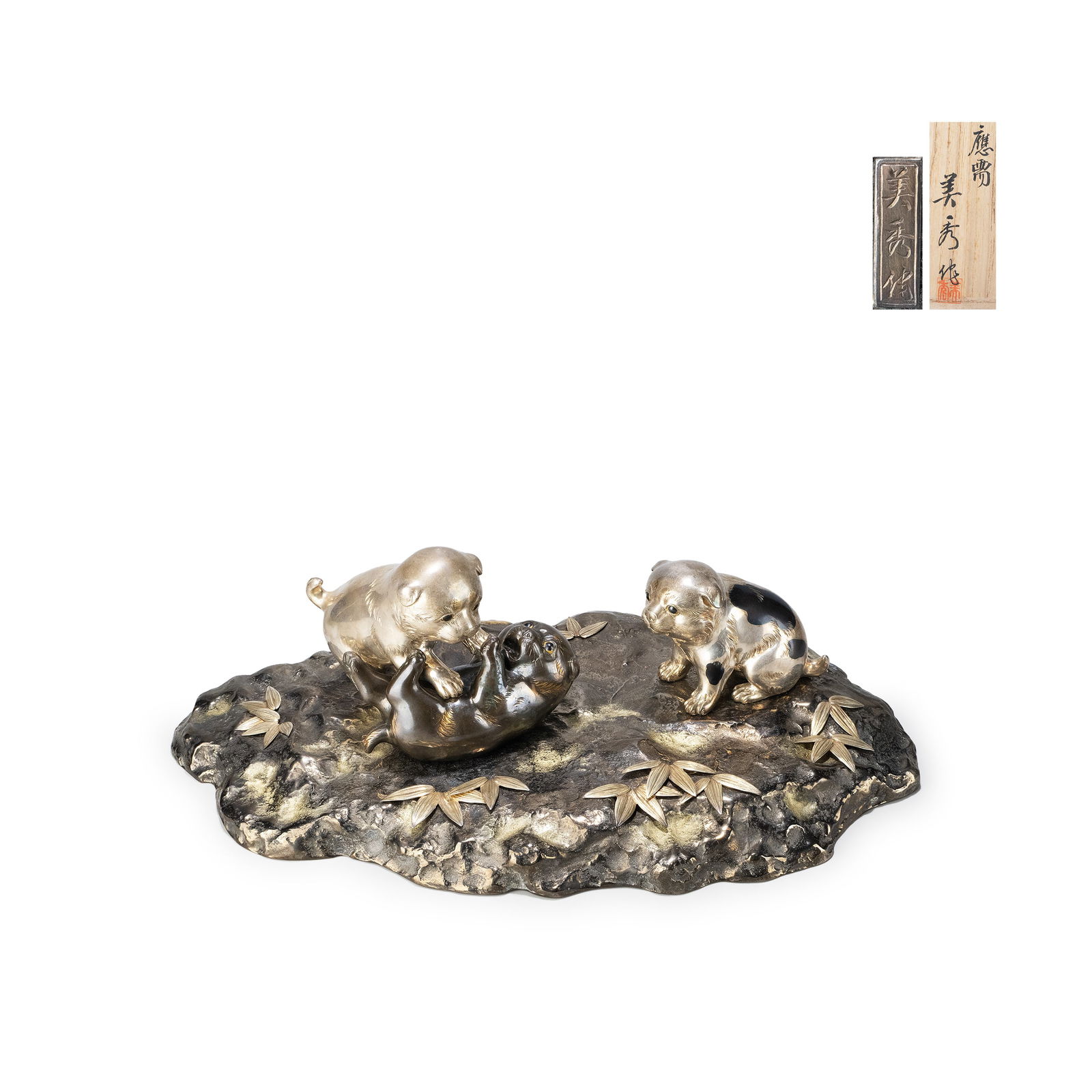 Silver Ornament ‘Dog ’ by Bishu: The composition depicts three playful puppies arranged dynamically upon a rocky base. One lies on its back in lively interaction, while another engages in play and the third observes, creating a balan
