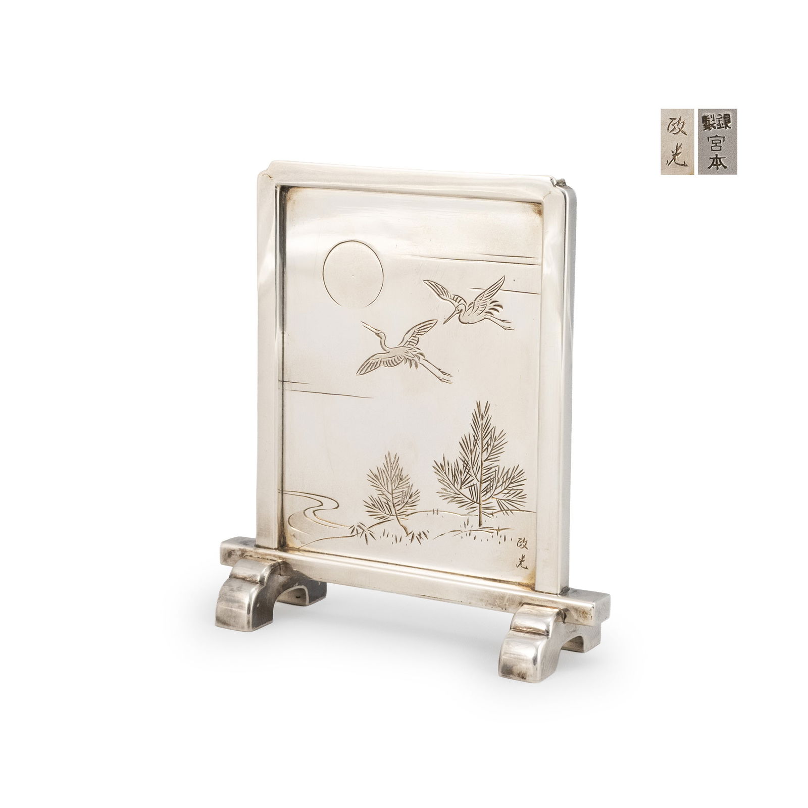 Silver Screen Made by Miyamoto: Of upright rectangular form set within a plain silver frame and raised on integral feet. The surface is finely engraved with a moonlit scene of two cranes in flight above pine trees beside flowing wat