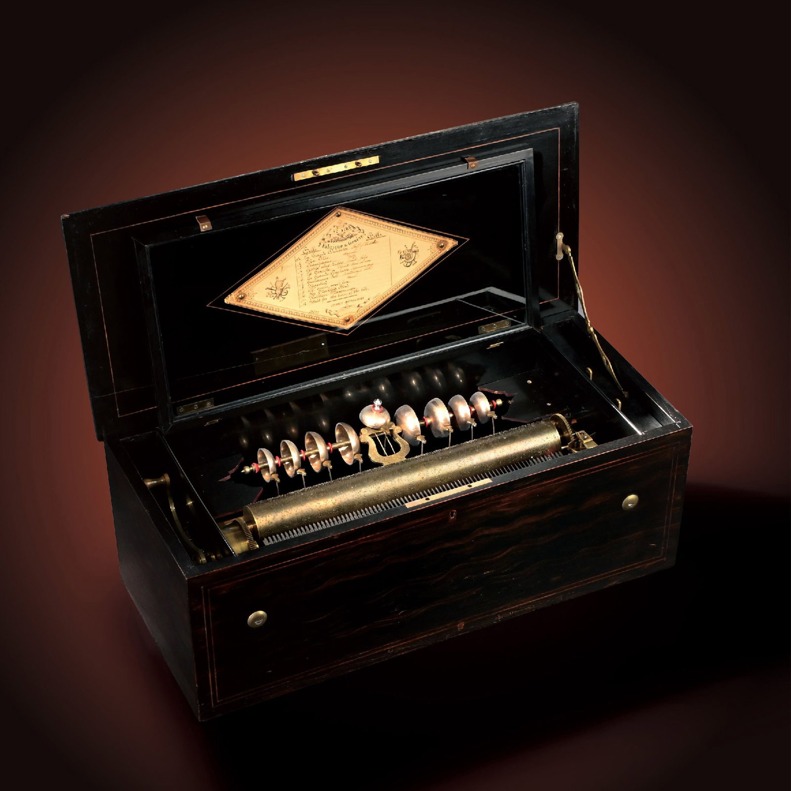 77-Note Comb 12Airs Music Box by Fabrique de Geneve: This fine cylinder music box, manufactured by Fabrique de Geneve, is fitted with a 77-tooth comb and housed in an elegant polished wooden case. The lid retains its original tune sheet, while the movem