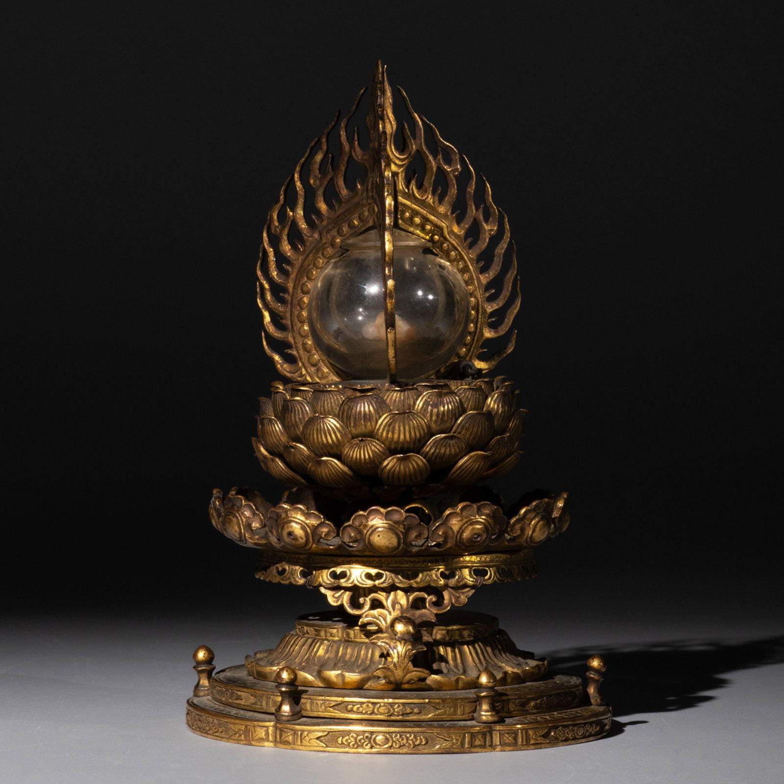 Gilt Bronze Stupa: This gilt bronze lotus reliquary stupa is executed in a dignified and elegant form. Rising from a multi-tiered lotus pedestal, the reliquary is surmounted by a flaming aureole that encloses a transpar