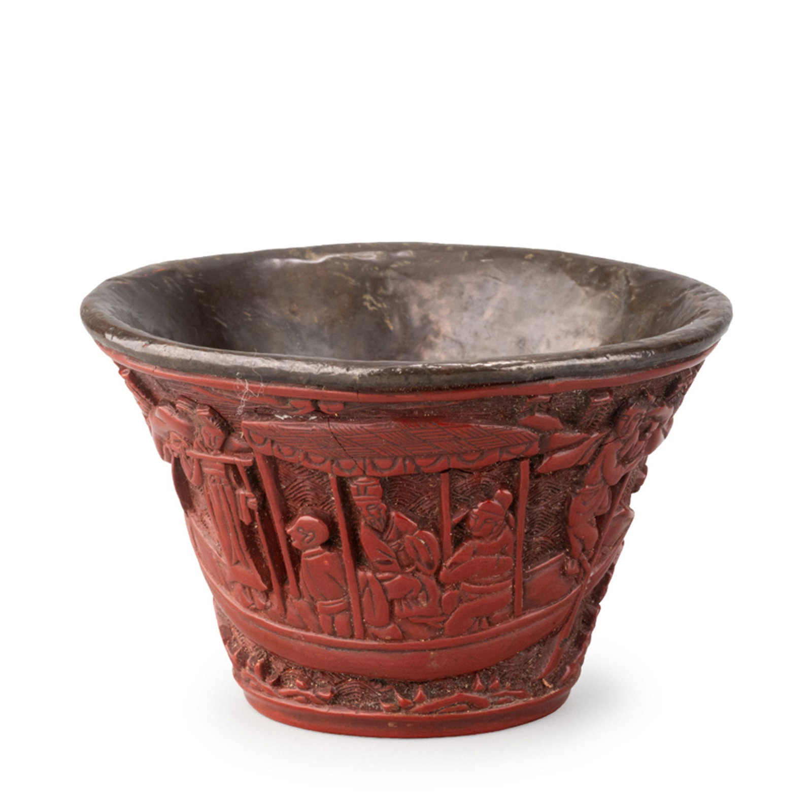 A carved cinnabar lacquer tea bowl: This carved cinnabar lacquer tea bowl is richly decorated with a continuous figural landscape executed in high relief. Scholars, attendants, pavilions, pine trees, rock formations, and boats are arran