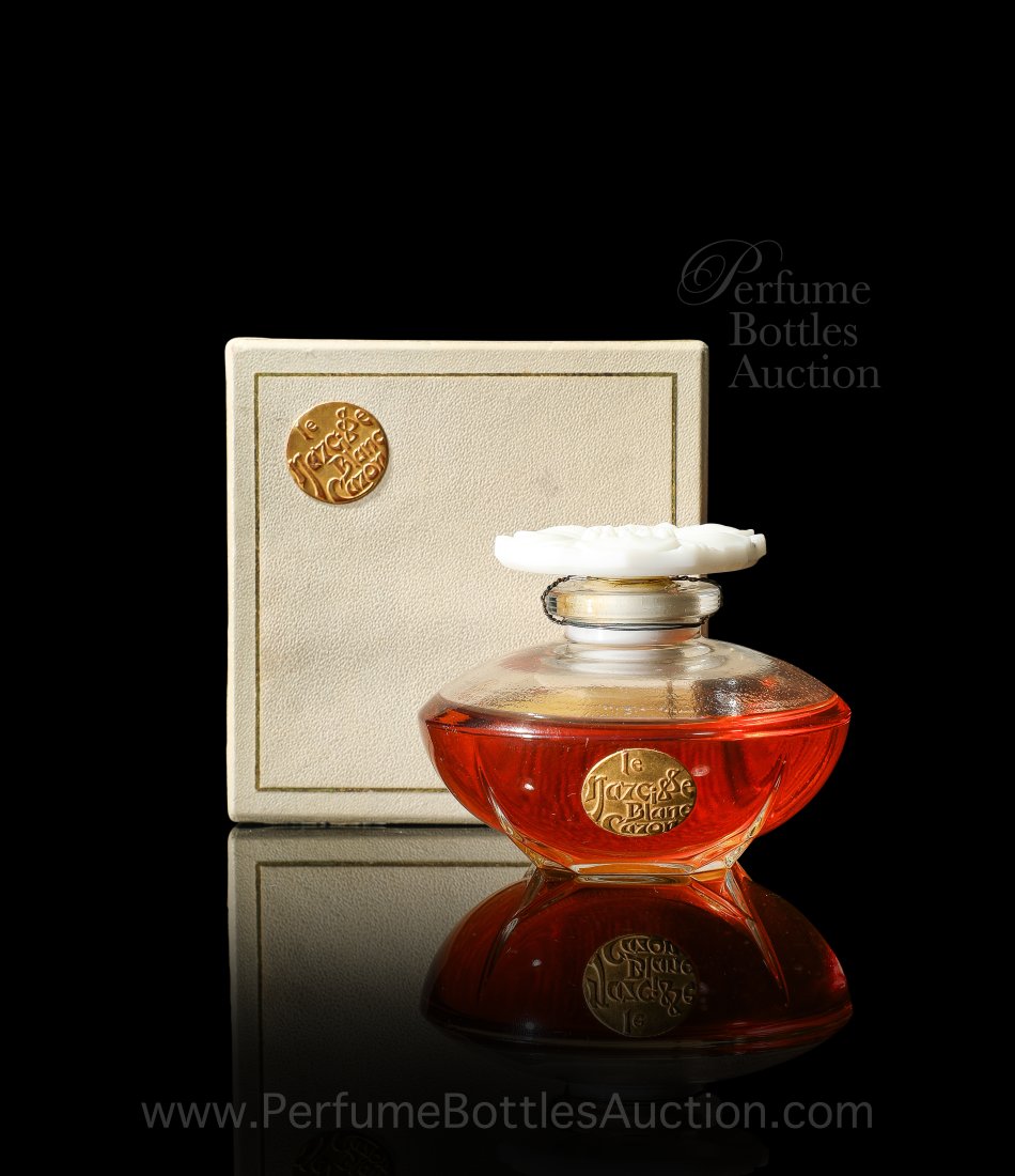 Caron Le Narcisse Blanc sealed perfume bottle: 1923 Verreries Brosse perfume bottle for Caron Le Narcisse Blanc, a clear glass circular form on square foot, white glass flower blossom stopper, cord seal, gilt label. Box with matching label. 2 1/4