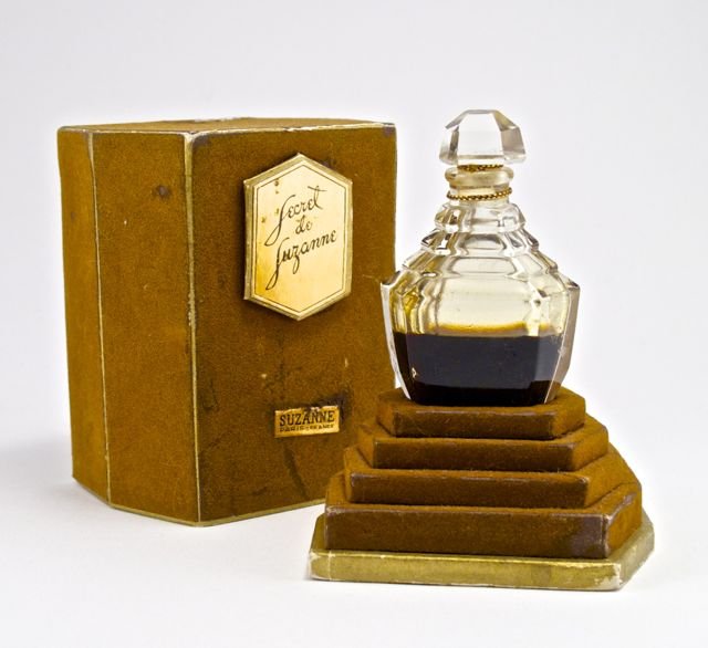 1924 Suzanne Secret de Suzanne perfume bottle and stopp: 1924 Suzanne Secret de Suzanne perfume bottle and stopper, clear glass, cord sealed, box (worn). 2 3/4 in.