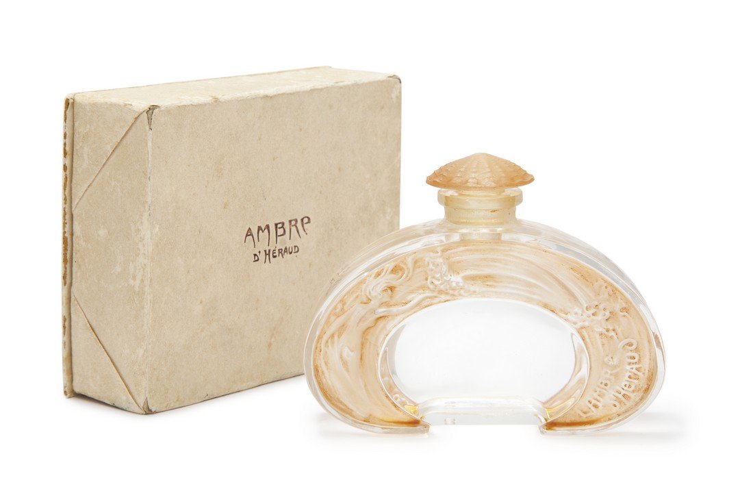 Lucien Gaillard "Ambre" perfume bottle: 1920 Lucien Gaillard for D’Heraud Ambre, clear glass perfume bottle and stopper, sepia patina, molded label, box. Sea motif of different mermaids each side, with figural shell stopper. 2 1/2 in.