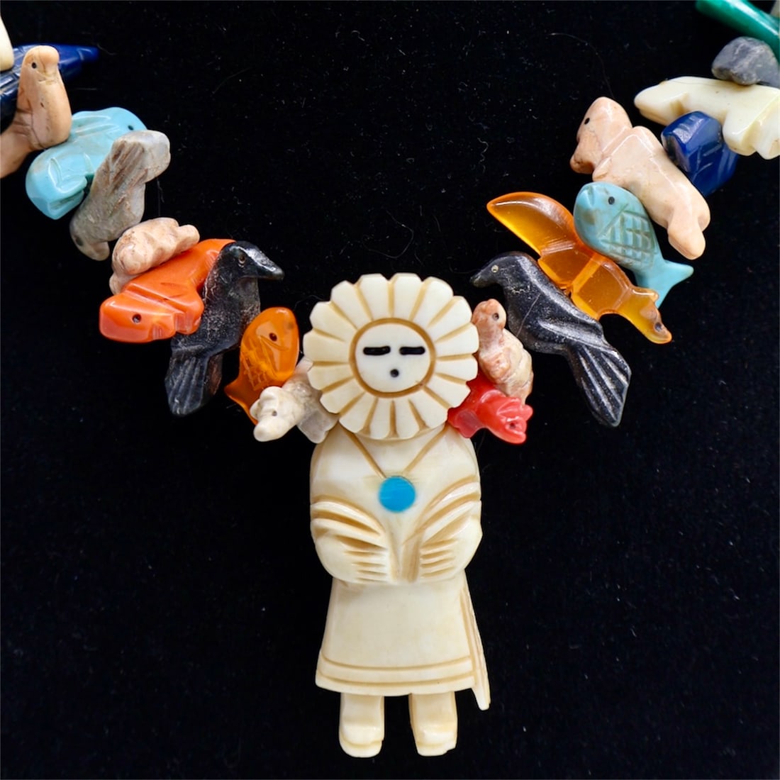 A Native American Zuni Bone Fetish Necklace: A fine vintage Zuni carved bone fetish necklace with abundant gemstone animals. A central sun face figure highlights the center with hand carved and inlaid detailing. 34” Long. Pendant Approxima