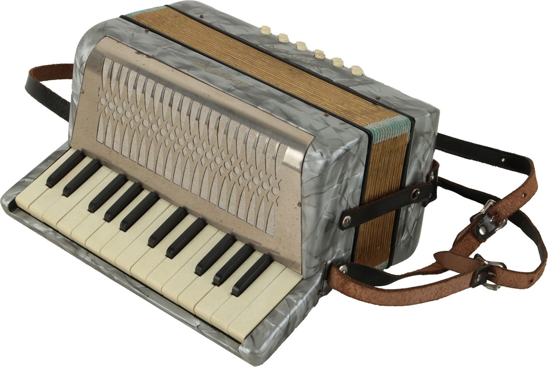 Hohner Mignon II Accordion: 25 keys, 12 bass. Keyboard 10.5". Grey marble finish with gold lettering, illustrated metal grille. Comes with leather strap. Made in Germany. Weight 2kg. Minor rust to grille.