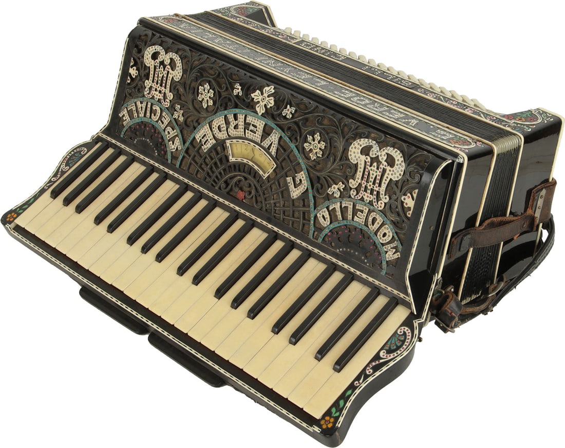 G. Verde Leyni Italia Billi Gino Accordion: 41 keys, 120 bass. Keyboard 19". 2 treble registers, 1 bass. Black finish decorated with colour illustrations and jewels, white and jewelled lettering. Comes with leather strap. Made in Italy. Weight