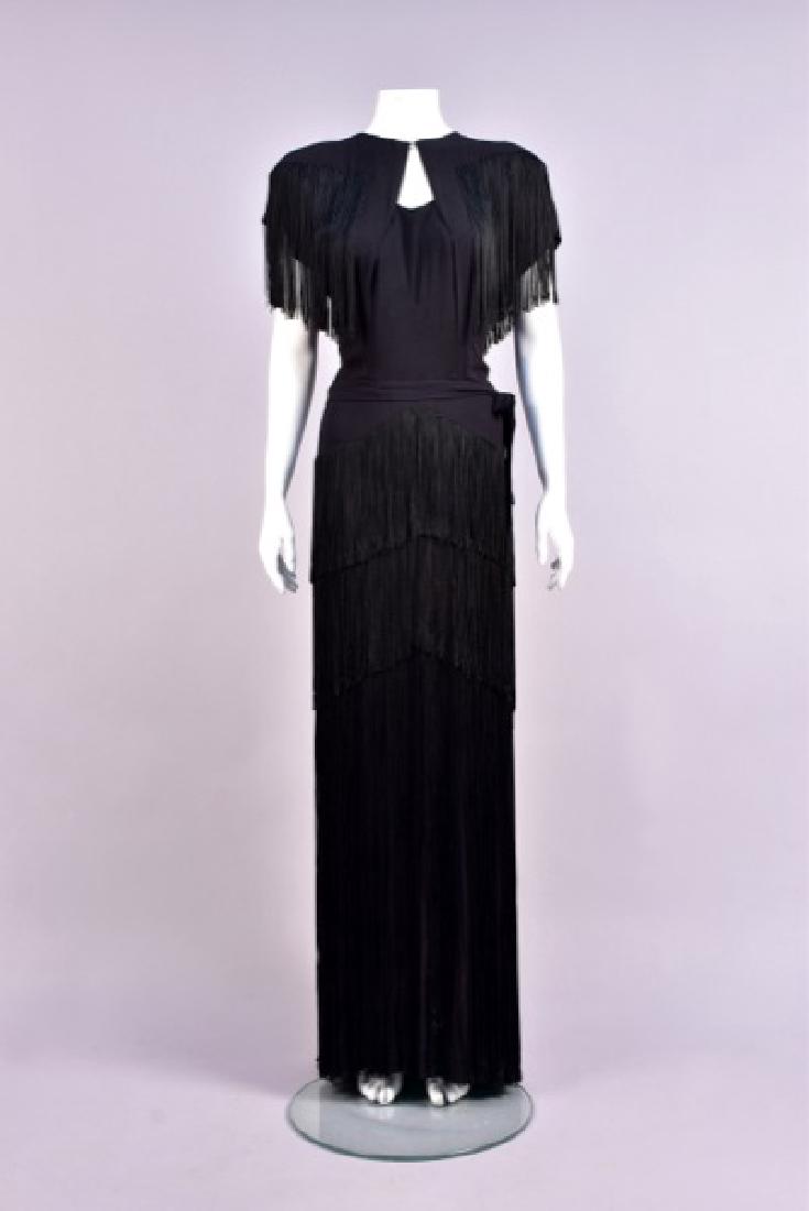 FRINGED CREPE EVENING DRESS, 1940s: Black silk with cap sleeve, jewel neckline with front keyhole, angled long fringe across padded shoulder forming a "V" on back, attached self sash, set-in waist, skirt having three tiers of fringe set