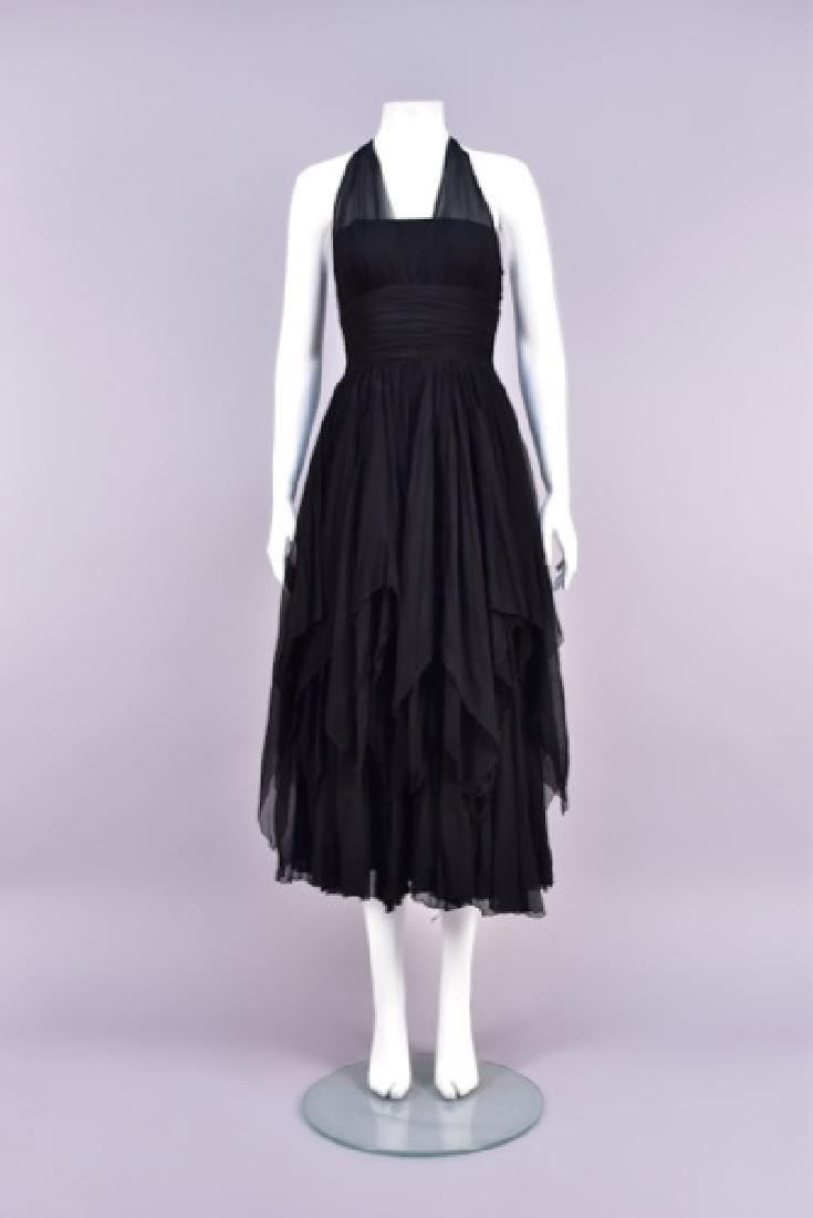 TRAINA NORELL BLACK CHIFFON HALTER GOWN, 1950s: Black silk fitted bodice with wide ruched waistband and sheer triangular panels forming halter, back center triangle over double silk cords, full layered skirt with shorter handkerchief points over lo