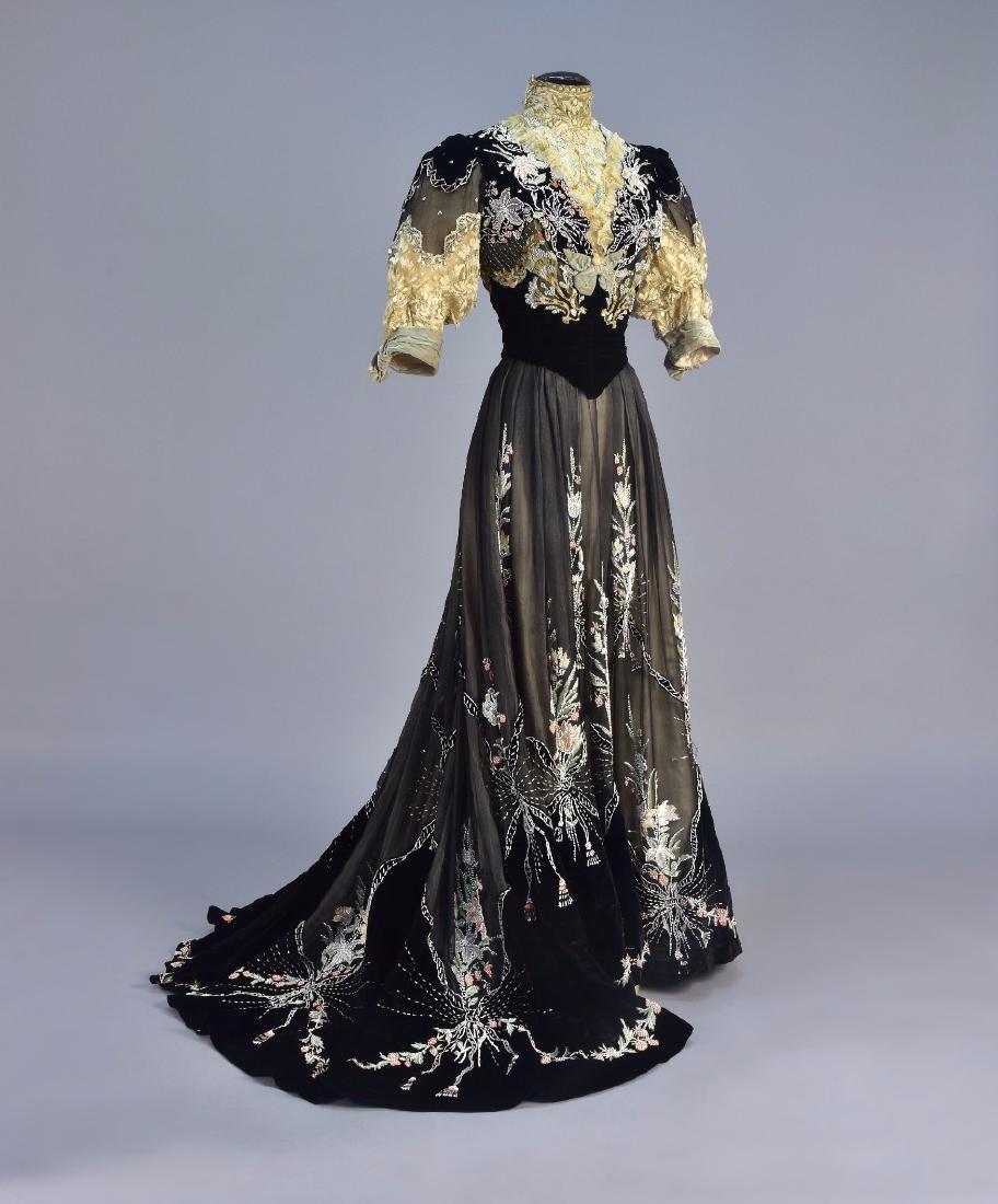 GUSTAVE BEER PARIS EMBROIDERED and BEADED GOWN, c. 1905: 2-piece black silk velvet and chiffon, boned bodice with bone silk lace high-neck insert and lower sleeve, decorated with white seed and bugle beads, blue lace, pastel silk satin stitch embroidery and