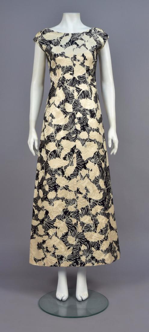 HATTIE CARNEGIE WARP PRINTED and BROCADE GOWN, c. 1960: Sleeveless warp printed floral silk in black and white brocaded with linear white flowers, boatneck and scoop back having crossed panels with four buttons, narrow A-line skirt. Labeled. B-34, W-28, H-