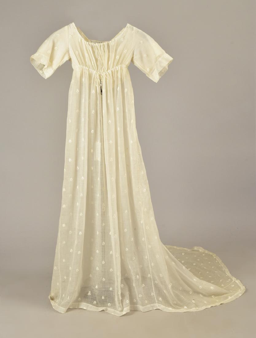 GRACE FLETCHER WEBSTER MUSLIN DRESS, 1805: Trained white cotton empire gown sprigged with satin-stitch floral devices, short sleeve drawstring bodice having two ties over crossed under-panels, slit back with tie above center pleats, long train