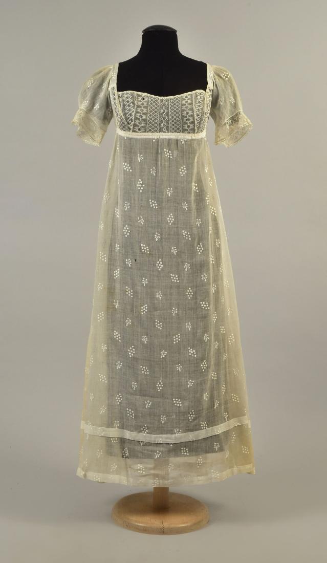 GRACE FLETCHER WEBSTER SPRIGGED MULL DRESS, 1808: White cotton having an empire bodice of embroidered net with short, puffed mull sleeve, net trim and back with drawstring ties and net inserts, slightly trained skirt covered in satin-stitch embroider