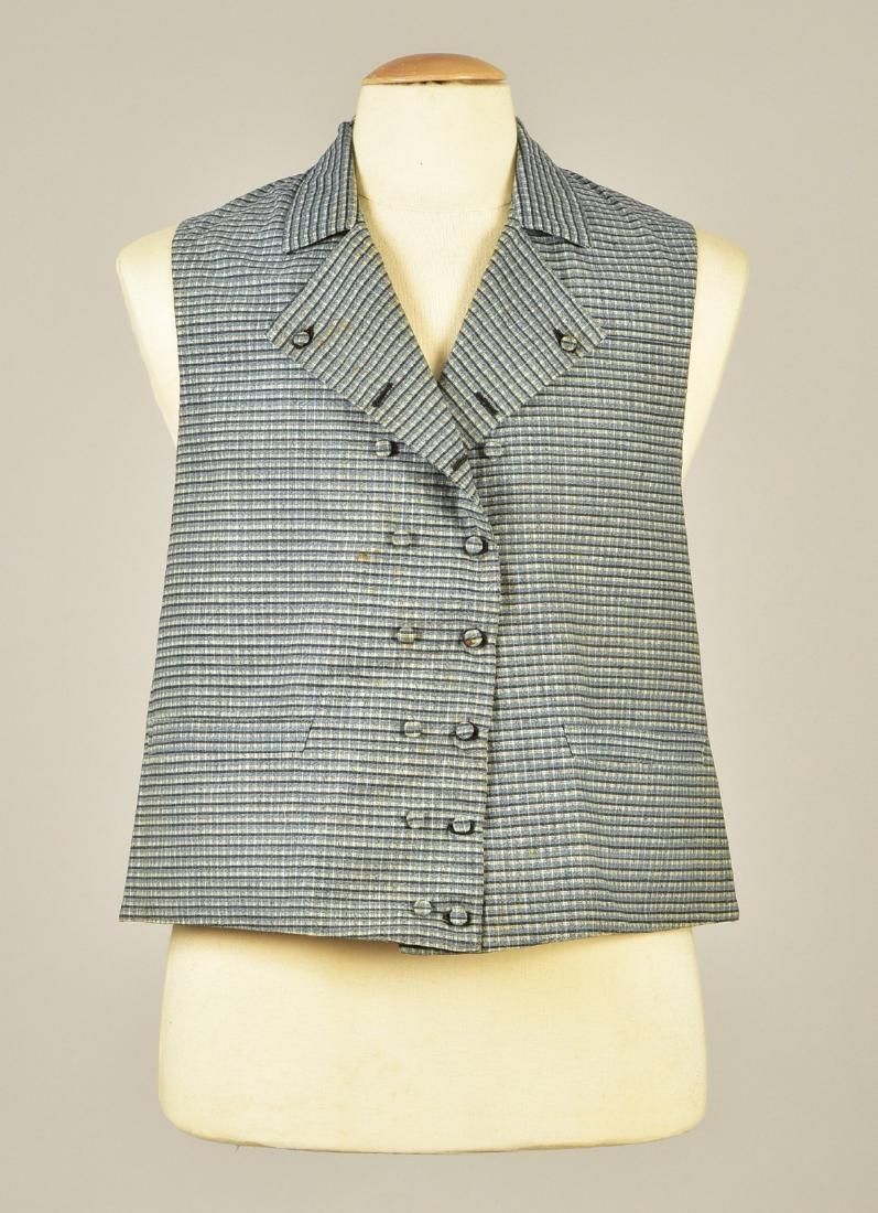 GENTLEMAN'S PLAID COTTON WAISTCOAT, c. 1810: Blue, black and white woven plaid having narrow double breast with self buttons and a pair of buttons to create optional lapels, stand collar, hemline pockets, white cotton back with two sets of ties,